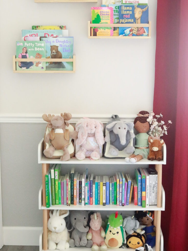 Moonkie Hug n Go toddler backpack (Elephant, Reindeer, Bunny) displayed in a child's room with books and other stuffed animals, showing them as a comforting part of toddler development.