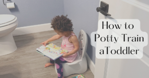 Toddler sits on a child-sized toilet in a bathroom, reading a colorful book.