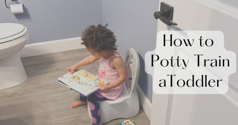 Toddler sits on a child-sized toilet in a bathroom, reading a colorful book.