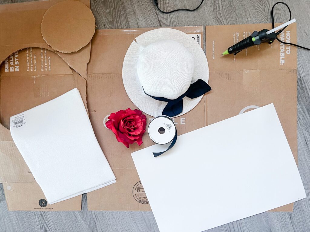 Supplies for a DIY Dionne hat including a white straw hat, glue gun, black ribbon, red rose, cardboard circles, and white foam sheets